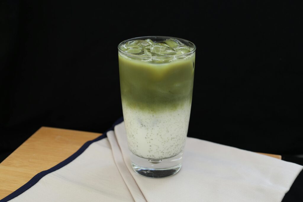 Refreshing iced matcha latte in a glass with milk on a wooden table.